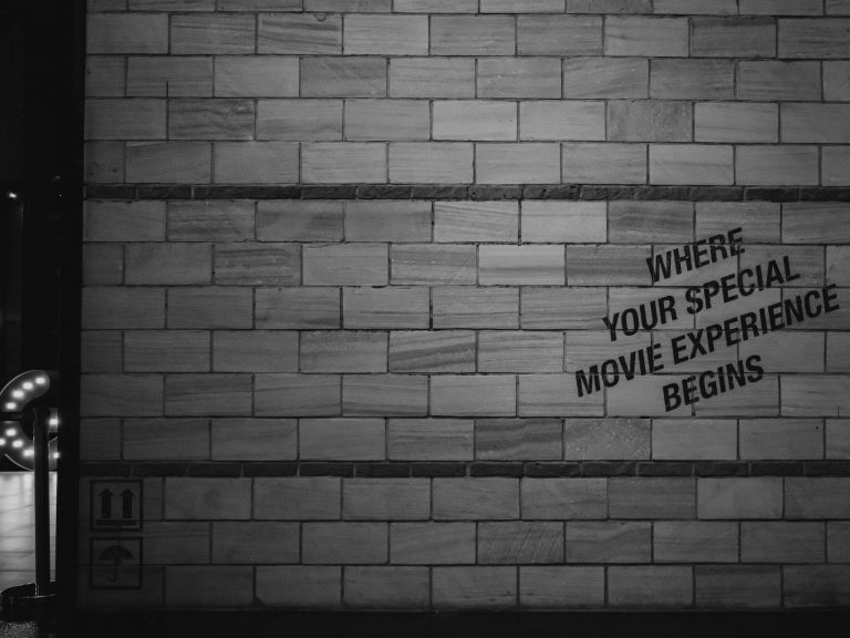 Black and white photo of a vintage movie theater sign on a brick wall.